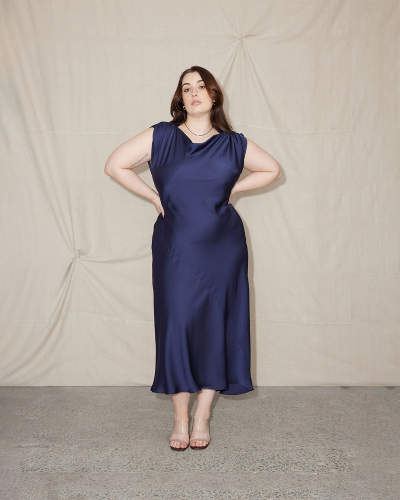 CURTIS MIDI DRESS MULHOLLAND NAVY | Bias cut cap sleeve midi dress crafted in a luxe Mulholland navy satin. This piece has ruched detail at the shoulder, a tie to cinch in the waist, and a...