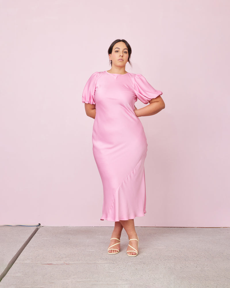 KENDALL SATIN DRESS CANDY | Bias cut satin midi dress with puff sleeves and a keyhole button closure at the back neck. The bias silhouette of this dress gently contours the body, while the satin...