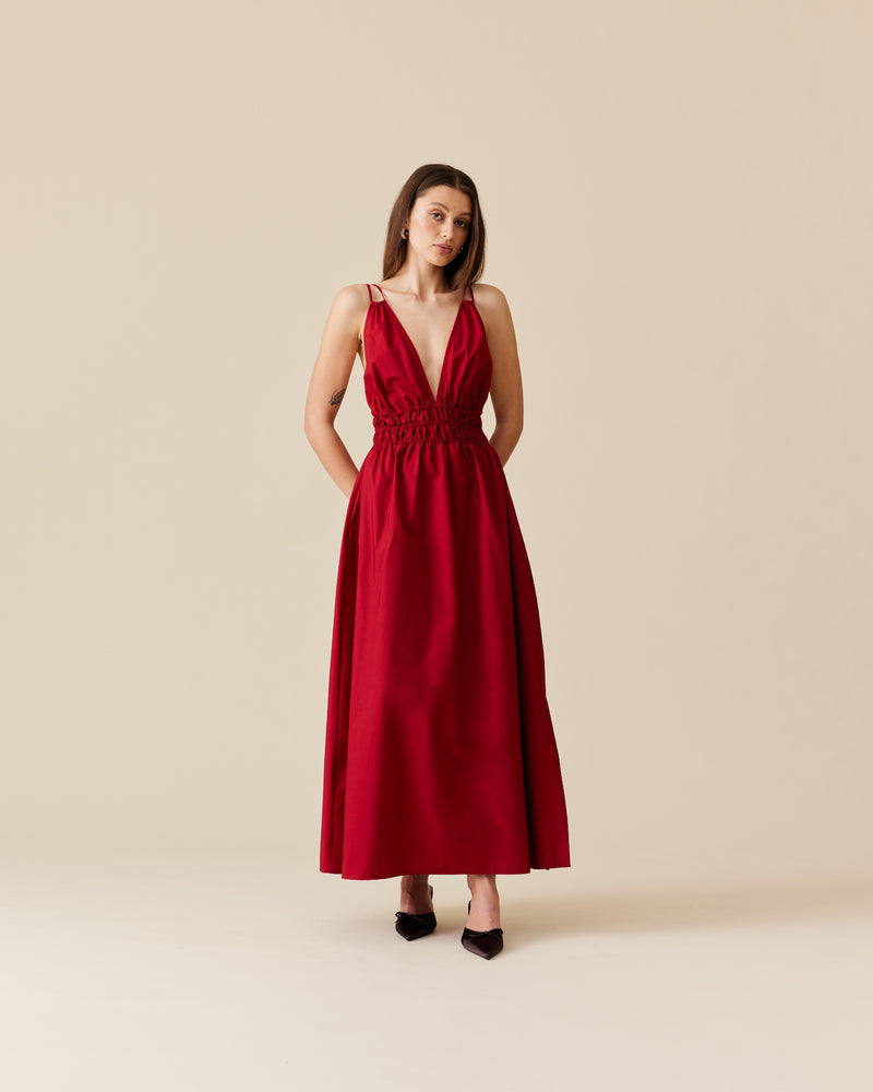 HERO MAXI DRESS GARNET | Double strap maxi dress with a plunge neckline, shirred waist detail, and side split in a garnet red cotton. The shirring at the waist accentuates the full skirt.
