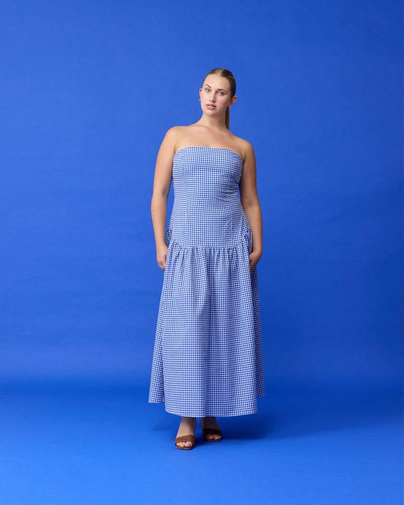 TRULLI MAXI DRESS COBALT GINGHAM | Cotton gingham maxi dress that is fitted through the body, then falls to a floaty basque style skirt. This dress features a dropped bodice-style waistline with a full skirt, and...